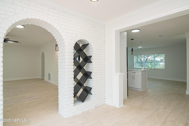 corridor featuring arched walkways, visible vents, light wood-style flooring, and baseboards