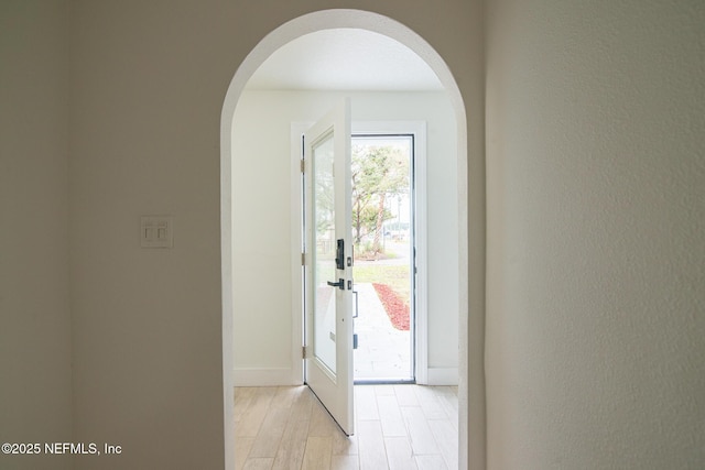 doorway with arched walkways, light wood-type flooring, and baseboards