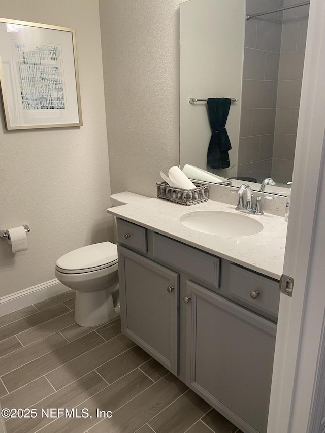 bathroom with wood finish floors, vanity, toilet, and baseboards