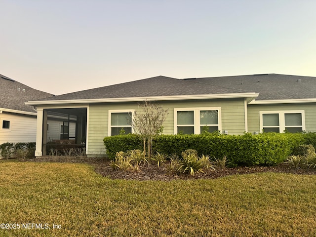 back of property featuring a shingled roof, a sunroom, and a yard