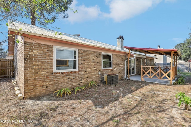 rear view of house featuring metal roof, a patio, brick siding, and fence