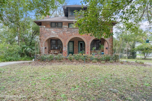 view of front of home featuring a front yard, a chimney, a porch, and brick siding