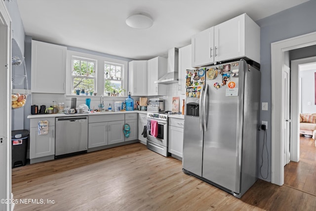 kitchen with stainless steel appliances, decorative backsplash, light wood-style floors, a sink, and wall chimney range hood