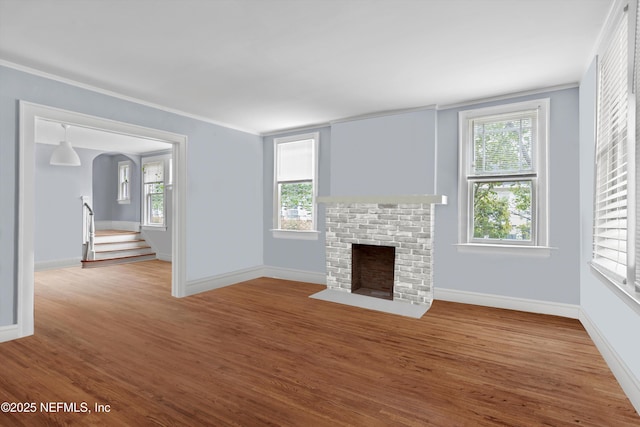 unfurnished living room with a healthy amount of sunlight, a fireplace, baseboards, and wood finished floors