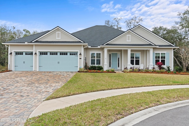 craftsman inspired home with a garage, a shingled roof, decorative driveway, and a front yard