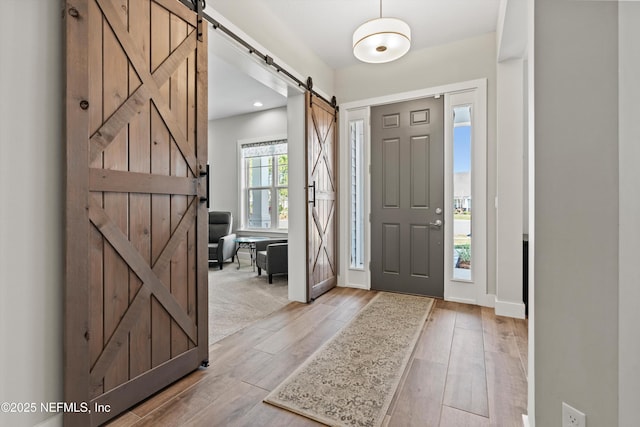 entrance foyer with light wood-type flooring, baseboards, and a barn door