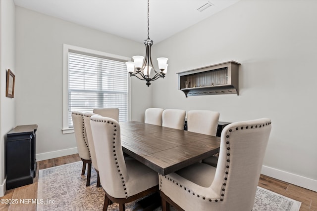 dining space with baseboards, visible vents, a chandelier, and wood finished floors