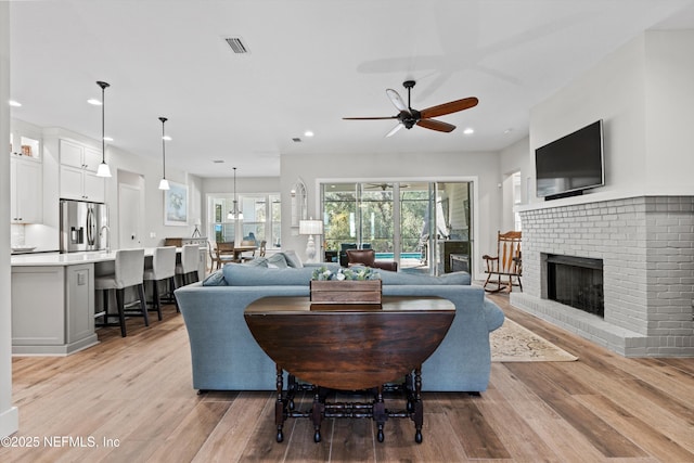 living room with recessed lighting, visible vents, light wood-style floors, a ceiling fan, and a brick fireplace