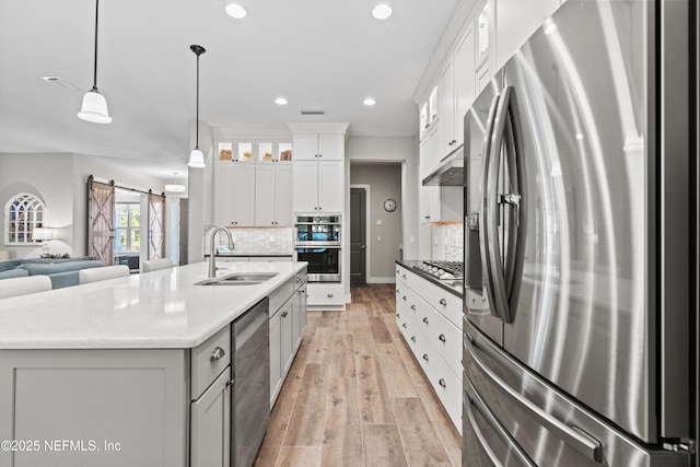 kitchen with a barn door, appliances with stainless steel finishes, open floor plan, light wood-type flooring, and a sink