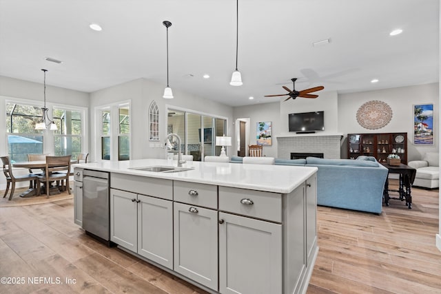 kitchen with a brick fireplace, dishwasher, gray cabinets, light wood-style floors, and a sink