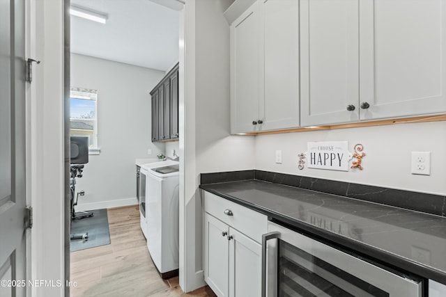 clothes washing area with wine cooler, cabinet space, light wood-style floors, independent washer and dryer, and baseboards