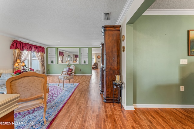 sitting room featuring a textured ceiling, wood finished floors, visible vents, and crown molding