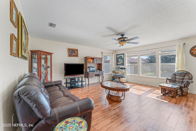 living room featuring ceiling fan, a textured ceiling, wood finished floors, and visible vents