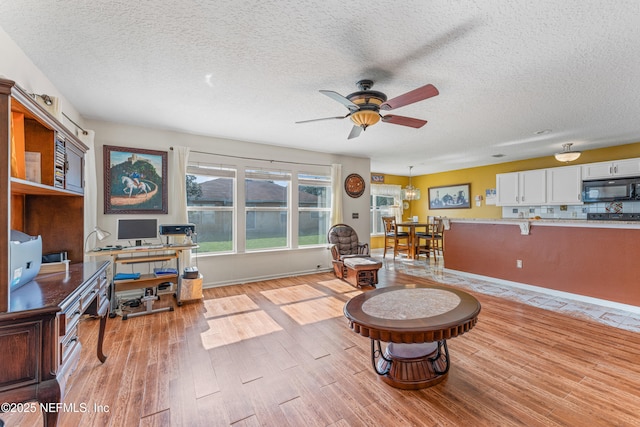 living room featuring a textured ceiling, baseboards, light wood-style flooring, and a ceiling fan