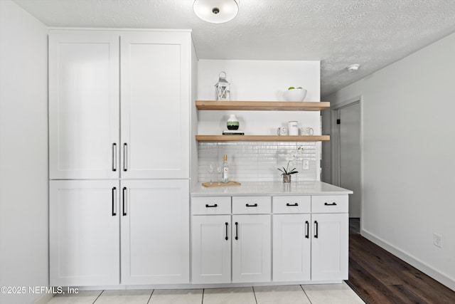 bar with a bar, baseboards, decorative backsplash, and a textured ceiling