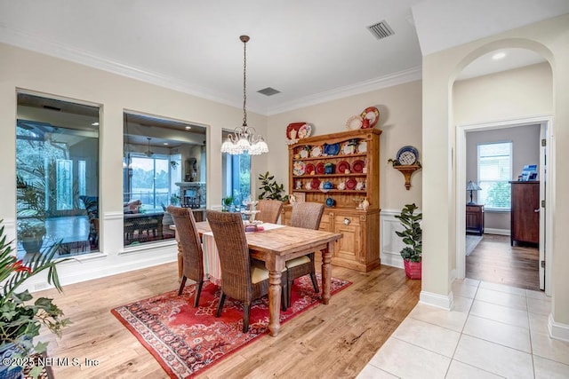 dining space featuring arched walkways, light wood finished floors, visible vents, and crown molding