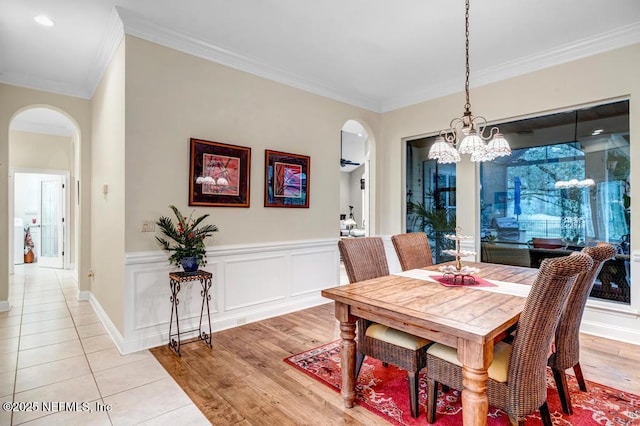 dining space with arched walkways, a wainscoted wall, light wood finished floors, a decorative wall, and ornamental molding