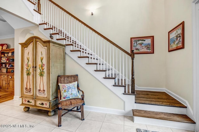 stairs featuring a towering ceiling, tile patterned flooring, baseboards, and ornamental molding