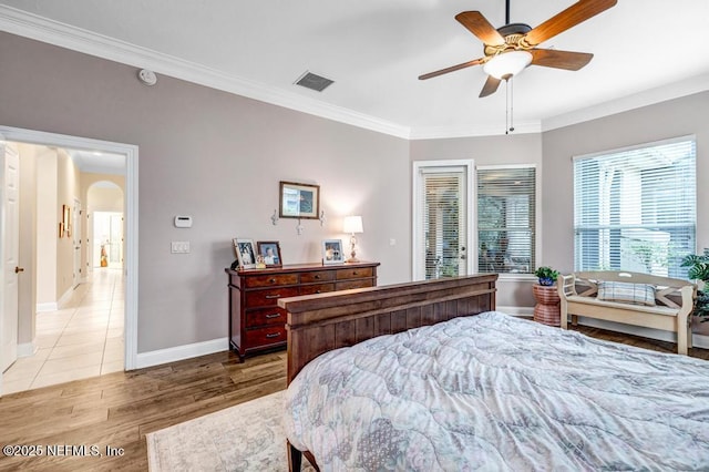 bedroom with arched walkways, crown molding, light wood finished floors, visible vents, and baseboards