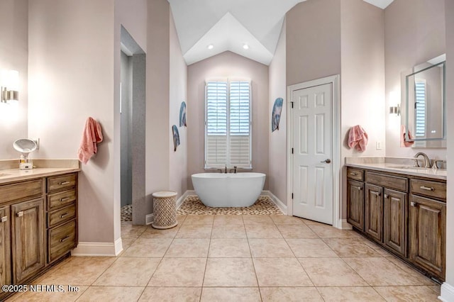 full bathroom with vaulted ceiling, vanity, a freestanding tub, baseboards, and tile patterned floors