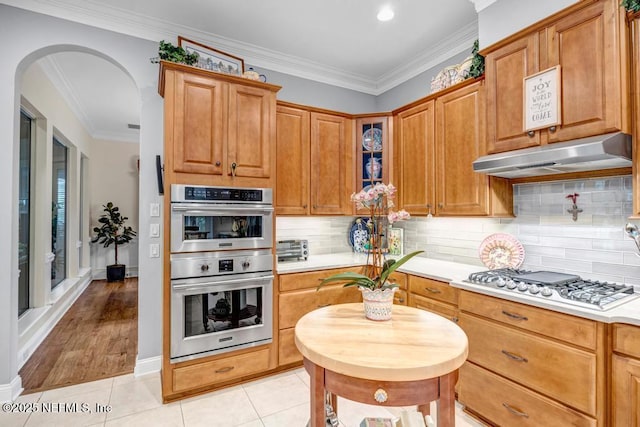 kitchen with arched walkways, appliances with stainless steel finishes, light countertops, under cabinet range hood, and light tile patterned flooring