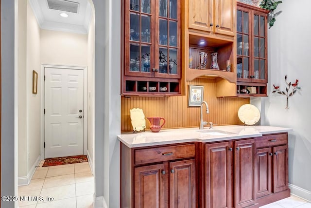 bar featuring light tile patterned floors, visible vents, baseboards, ornamental molding, and a sink