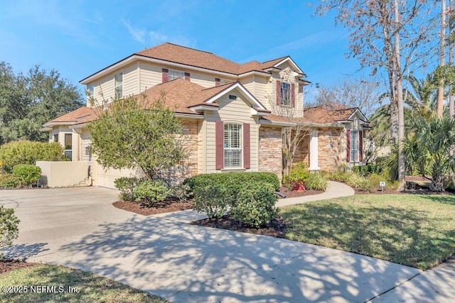 view of front of house with stone siding, a front lawn, roof with shingles, and driveway