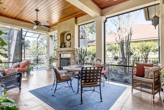 sunroom with an outdoor stone fireplace, wood ceiling, and a ceiling fan