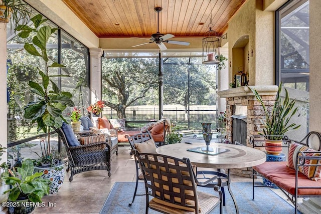 sunroom with wood ceiling, an outdoor stone fireplace, and a ceiling fan