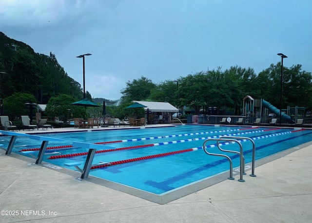 pool featuring fence, playground community, and a patio