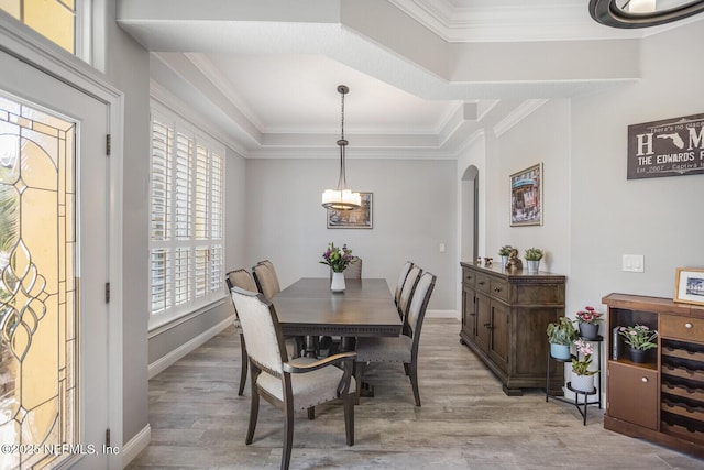 dining room featuring arched walkways, a raised ceiling, ornamental molding, and wood finished floors