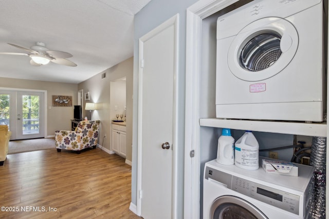 laundry room featuring a ceiling fan, baseboards, french doors, stacked washing maching and dryer, and light wood finished floors