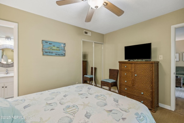 carpeted bedroom featuring visible vents, ensuite bath, ceiling fan, a sink, and a closet