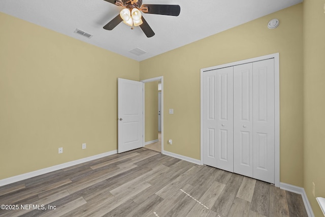 unfurnished bedroom featuring baseboards, a closet, visible vents, and wood finished floors