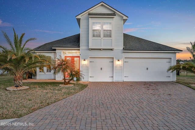 view of front facade with a garage, a front lawn, decorative driveway, and a shingled roof