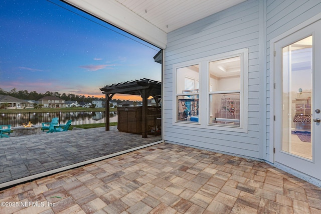 patio terrace at dusk with a water view, an outdoor fire pit, fence, and a pergola