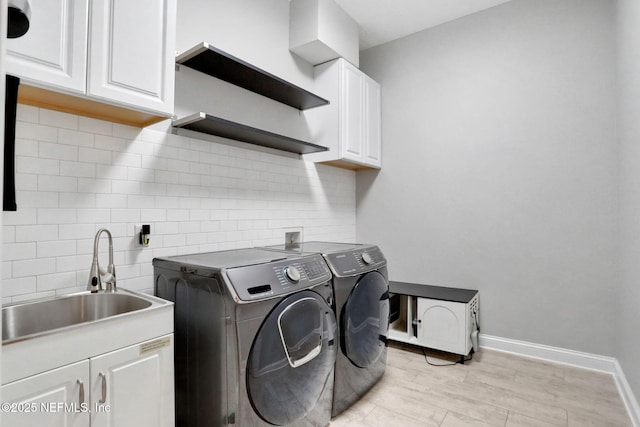 laundry room featuring a sink, light wood-style floors, baseboards, cabinet space, and washing machine and clothes dryer