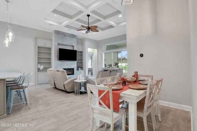 dining area with light wood-style flooring, a large fireplace, coffered ceiling, and a towering ceiling