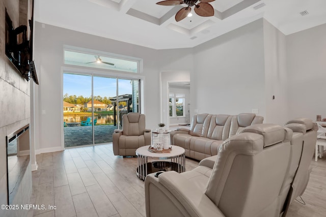 living area featuring visible vents, coffered ceiling, a tiled fireplace, ceiling fan, and a high ceiling