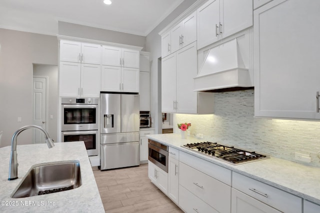 kitchen with stainless steel appliances, a sink, white cabinetry, backsplash, and custom range hood