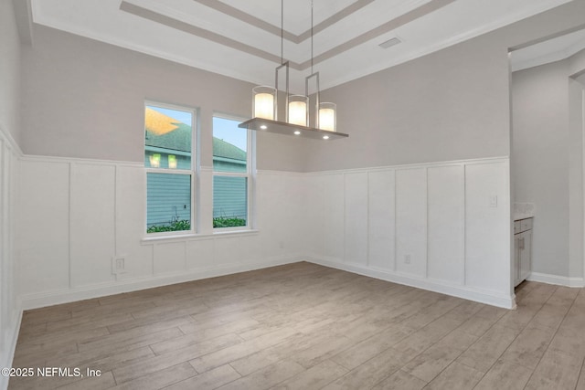 spare room with visible vents, a tray ceiling, light wood-style flooring, and a decorative wall