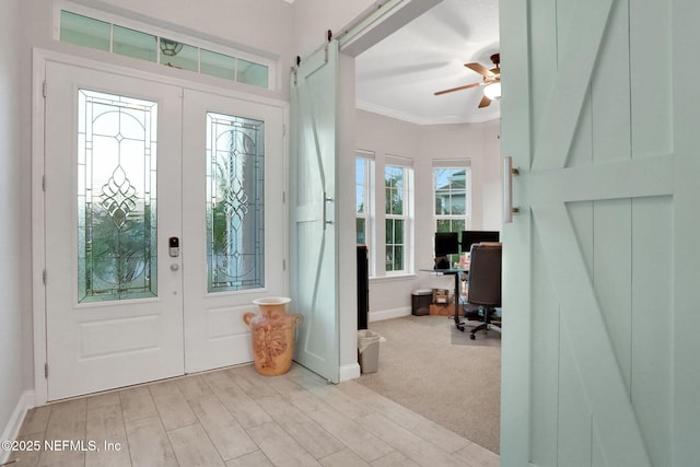 foyer with a barn door, light wood-style floors, baseboards, french doors, and ornamental molding