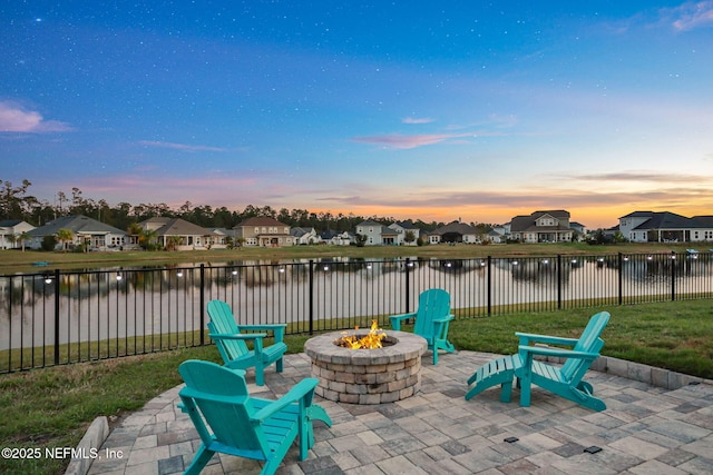 patio terrace at dusk featuring an outdoor fire pit, a fenced backyard, a residential view, and a water view