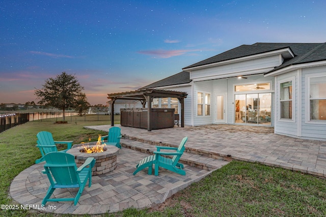 patio terrace at dusk with a lawn, a hot tub, an outdoor fire pit, a pergola, and fence private yard