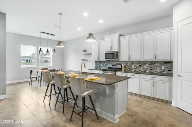 kitchen with stainless steel appliances, a sink, a kitchen breakfast bar, decorative backsplash, and dark countertops