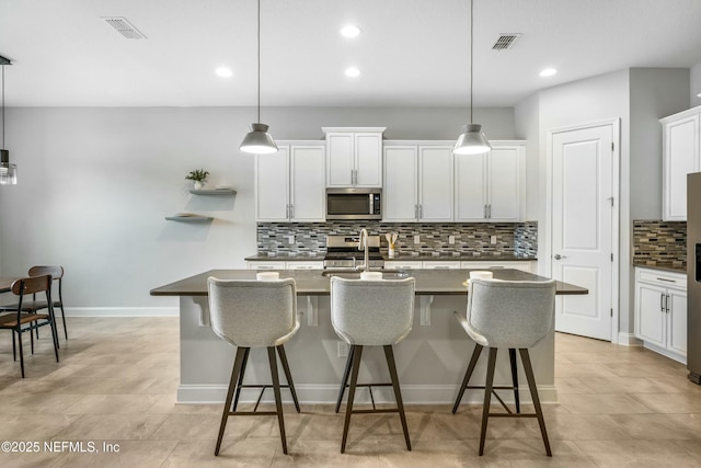 kitchen featuring appliances with stainless steel finishes, dark countertops, visible vents, and a breakfast bar area