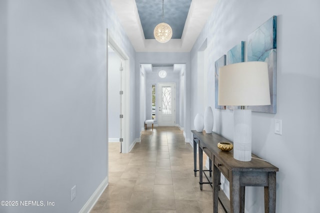 corridor with light tile patterned floors, baseboards, and an inviting chandelier