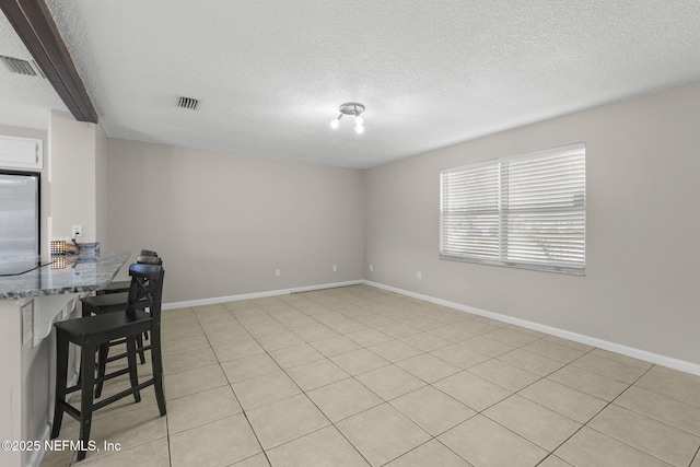 unfurnished dining area with visible vents, a textured ceiling, and baseboards