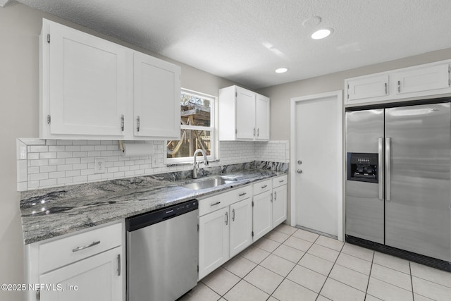 kitchen featuring light stone counters, appliances with stainless steel finishes, white cabinets, and a sink