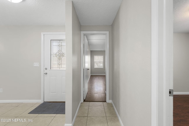 hall featuring baseboards, a textured ceiling, and light tile patterned flooring